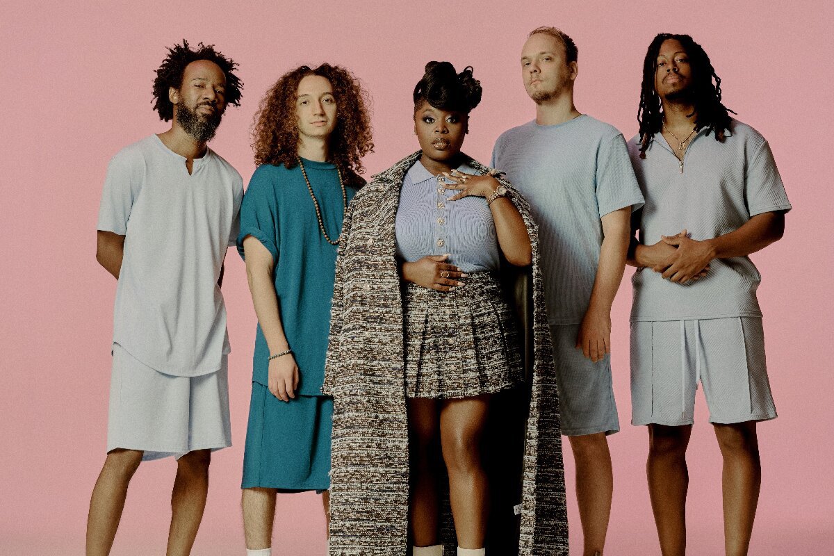 Five members of Tank and The Bangas standing against a pink backdrop in pastel and teal outfits