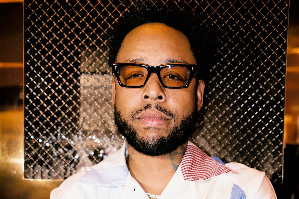Close-up portrait of Terrace Martin in amber-tinted glasses in front of a metal mesh panel