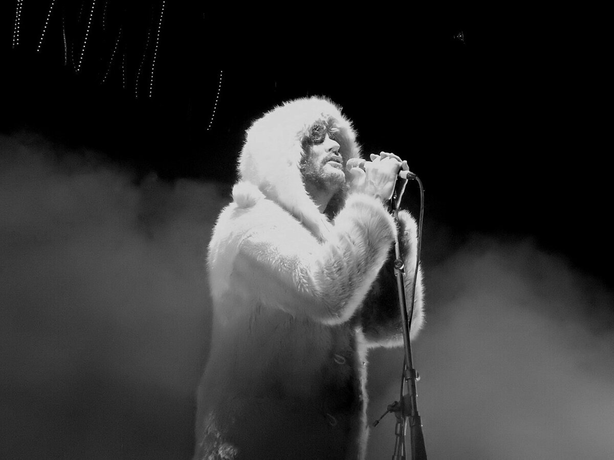 Singer in a white hooded fur coat holding a microphone in stage smoke