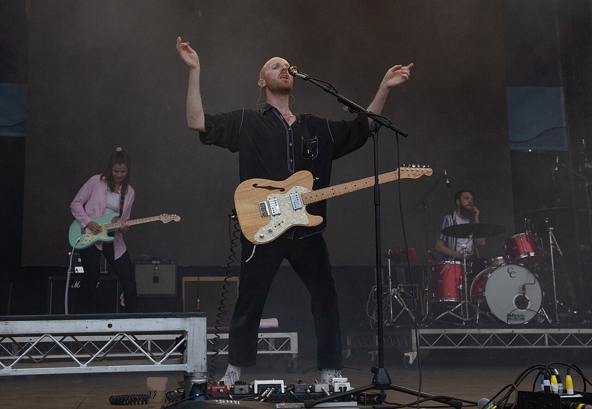 Singer-guitarist with arms raised at the microphone, with a guitarist and drummer on stage behind him