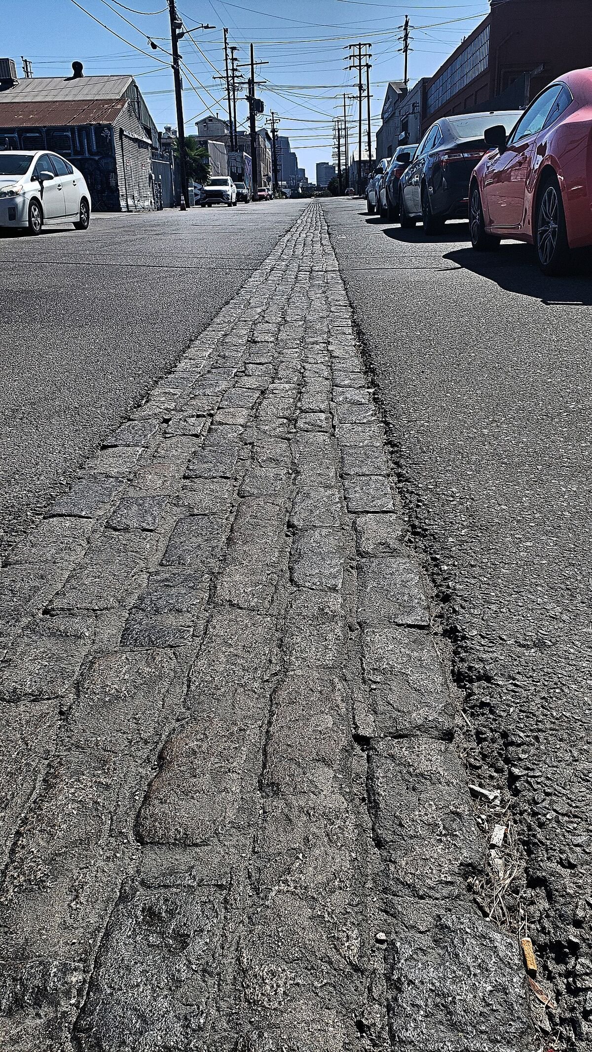 Cobblestone strip down the middle of Naud Street in Chinatown with parked cars and downtown buildings in the distance