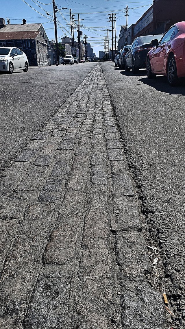 Cobblestone strip down the middle of Naud Street in Chinatown with parked cars and downtown buildings in the distance