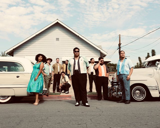Members of Thee Sinseers posed on a residential street in front of vintage cars