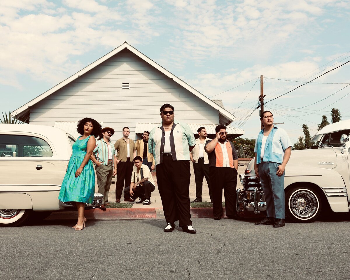 Members of Thee Sinseers posed on a residential street in front of vintage cars