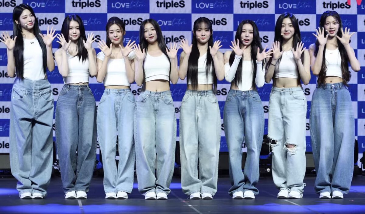Members of tripleS standing in a row with hands raised in front of a tripleS backdrop at a showcase