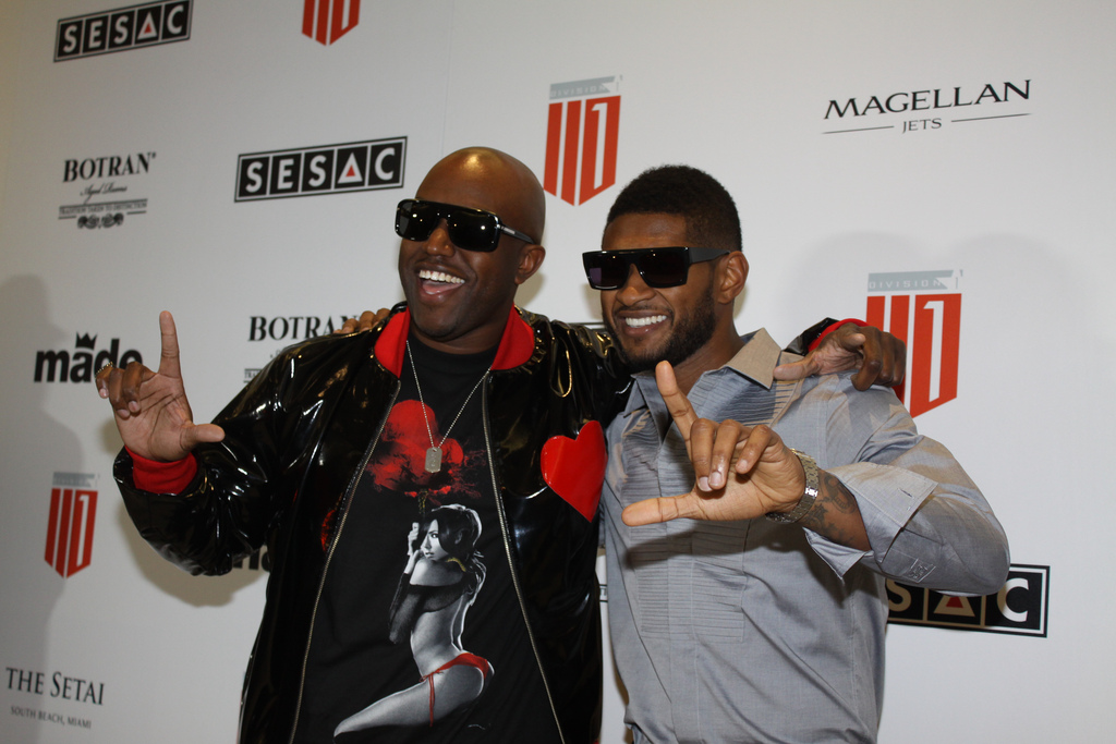 Usher in sunglasses and a gray shirt posing with songwriter Rico Love on a sponsor step-and-repeat
