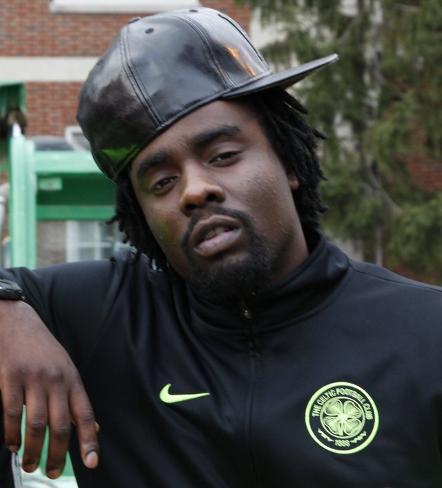 Close-up portrait of rapper Wale in a black leather cap and black zip jacket, leaning on his arm