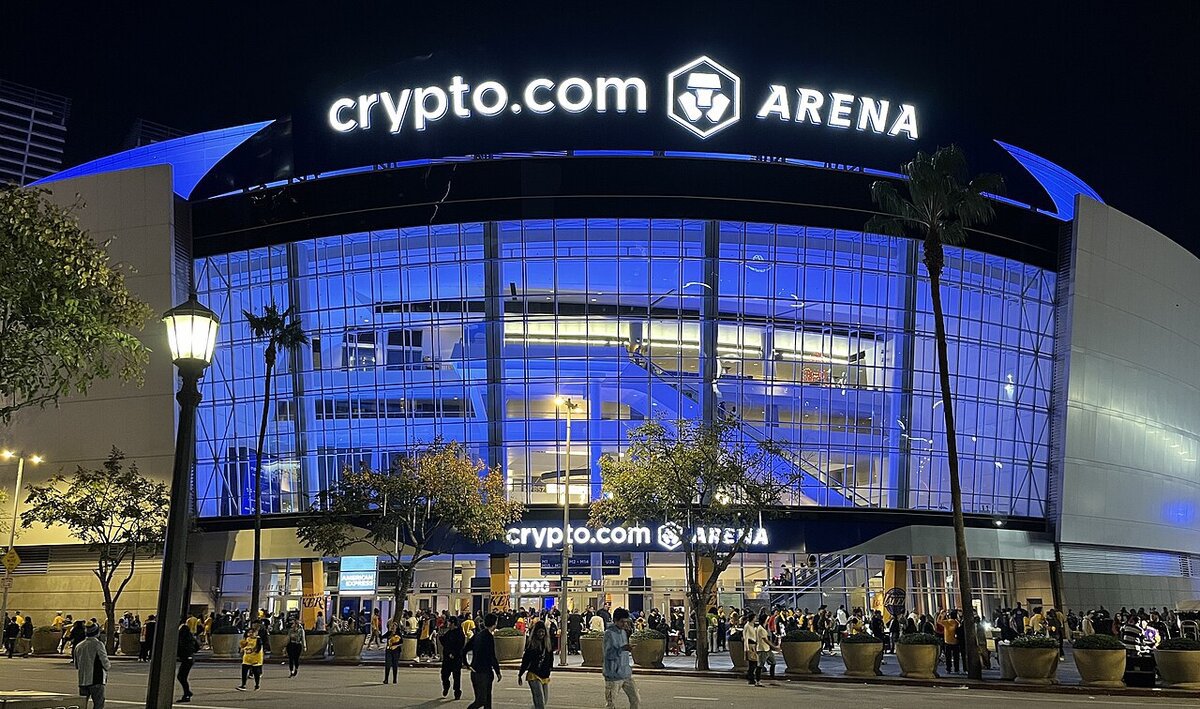 Crypto.com Arena in Downtown Los Angeles lit in blue at night, with fans walking past the entrance