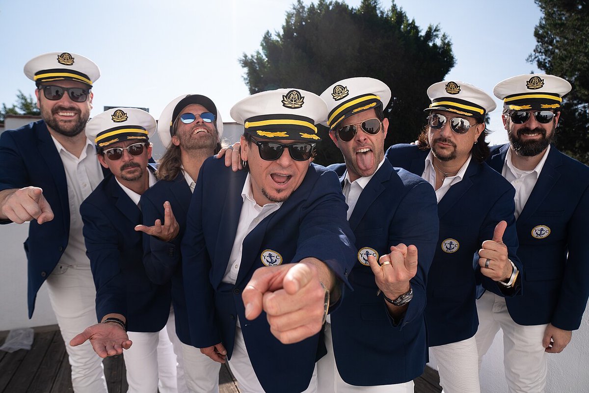 Seven members of Yachtley Crew in navy blazers and captain's hats, pointing at the camera