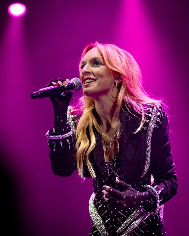 Zolita singing into a microphone under magenta stage lights