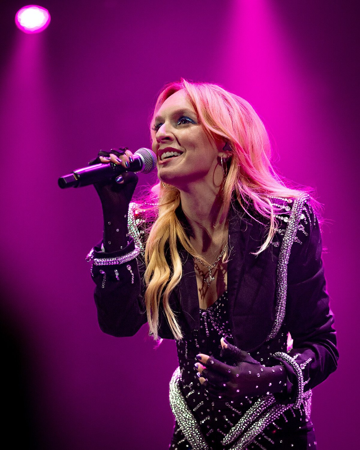 Zolita singing into a microphone under magenta stage lights