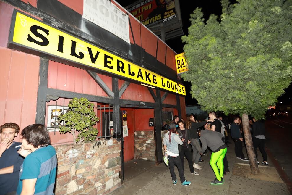Yellow Silverlake Lounge sign over a red-painted storefront at night, with a small crowd gathered on the sidewalk outside
