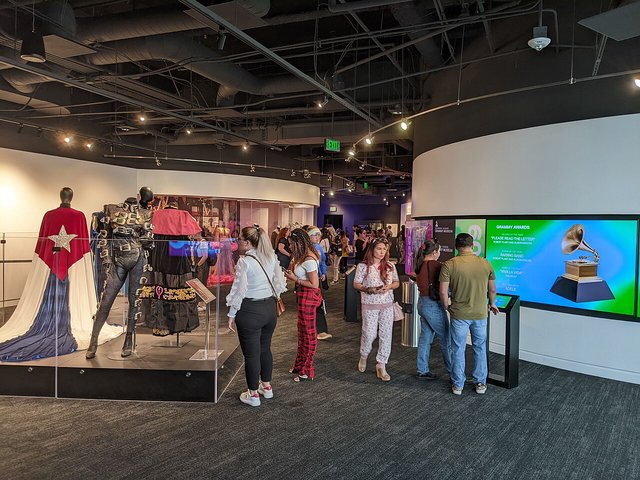 Visitors browsing costume displays and a Grammy Awards screen inside the Grammy Museum in Los Angeles