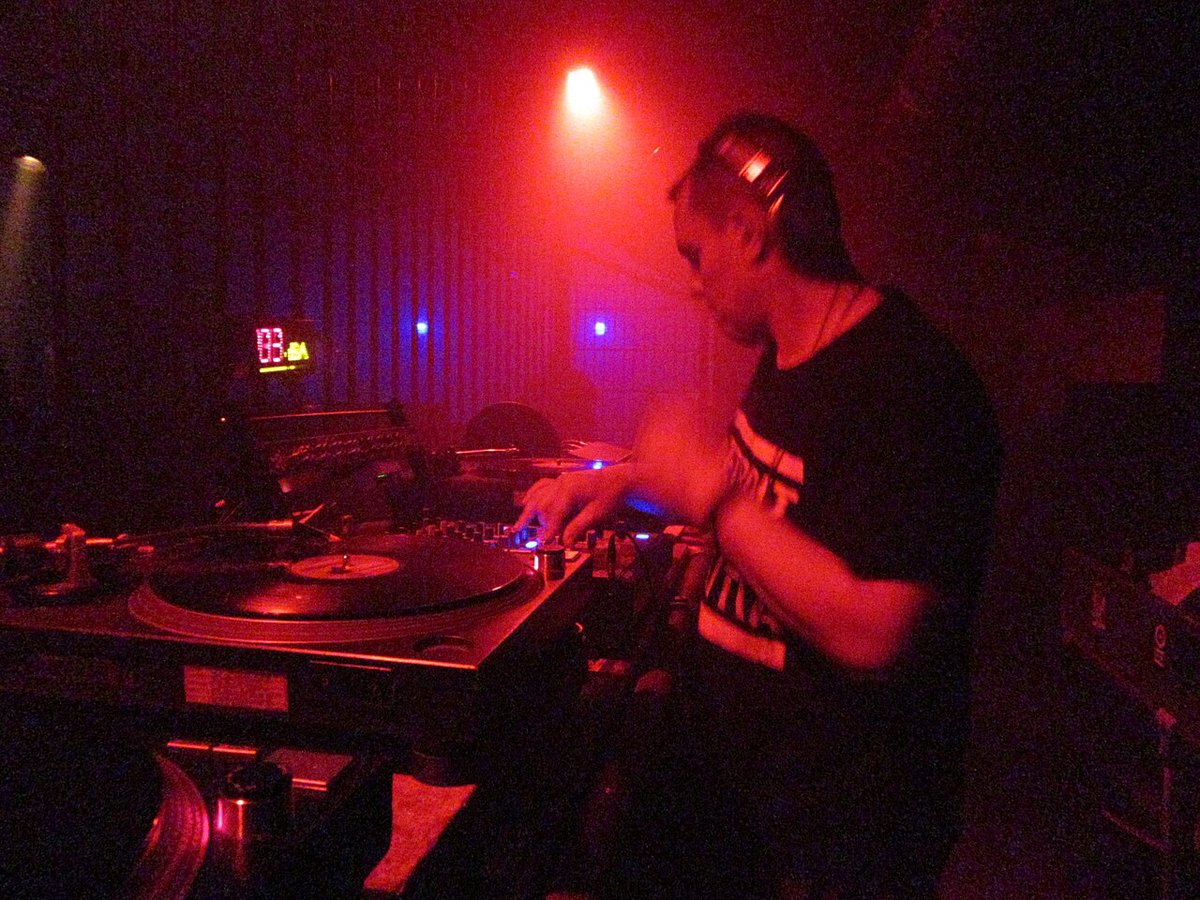 A DJ in a dark club mixing on turntables under red and magenta light