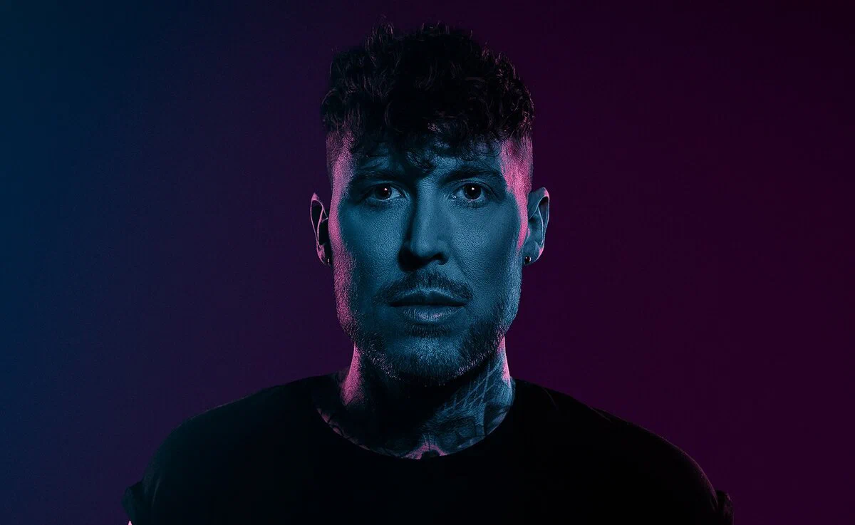 Ben Nicky lit in blue against a dark pink backdrop in a promo portrait