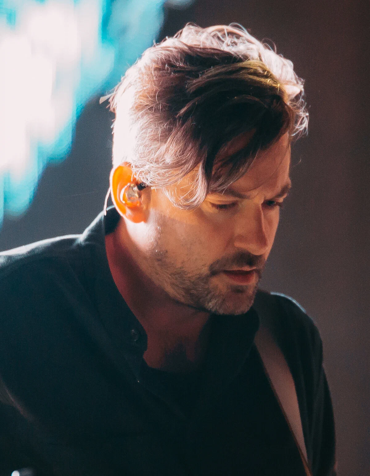 Bonobo in a dark shirt and an in-ear monitor, looking down while performing on stage at Roskilde Festival
