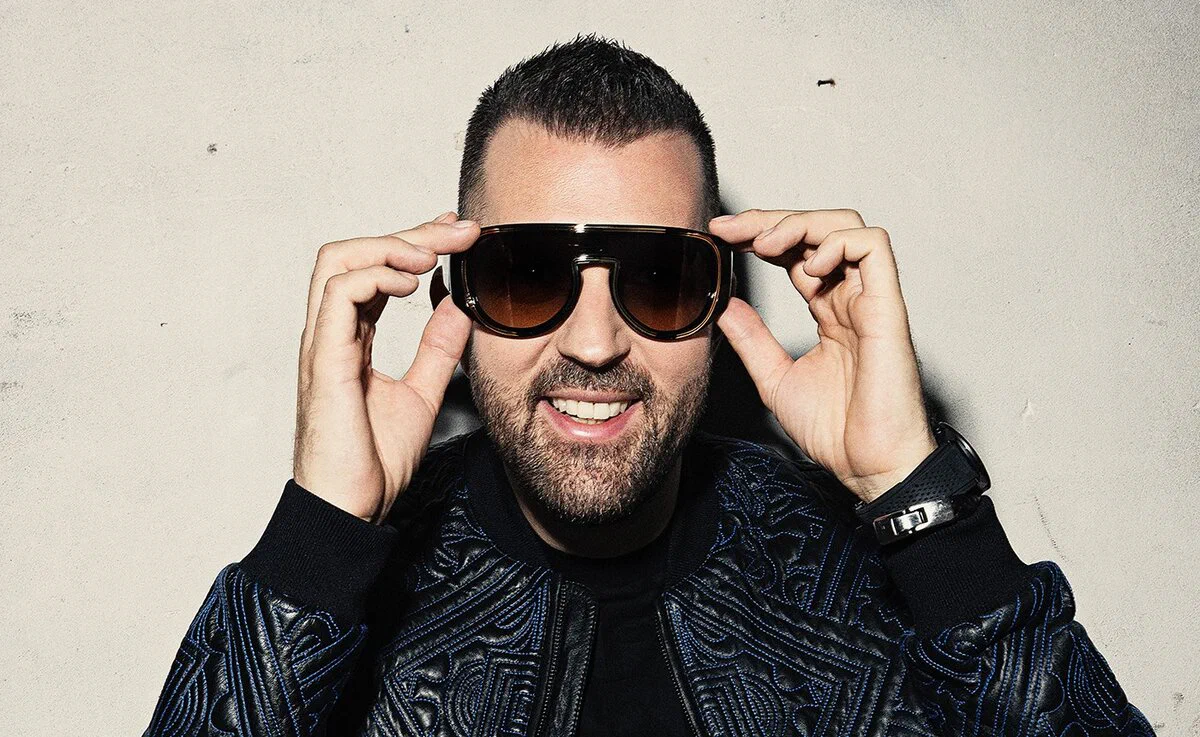 Brennan Heart holding sunglasses on his face in a promo portrait