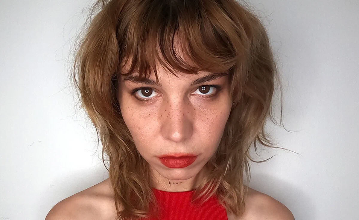 Mija with tousled hair and red lipstick in a close promo portrait