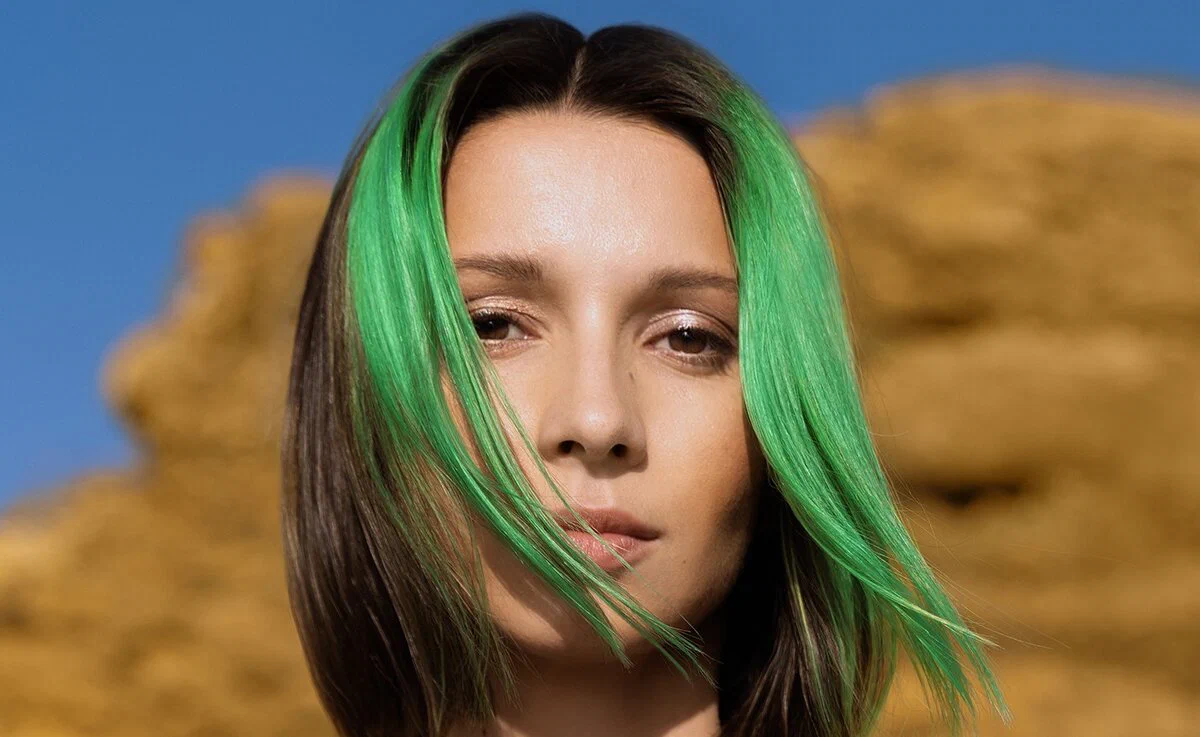 Miss Monique with green-streaked hair in a close promo portrait