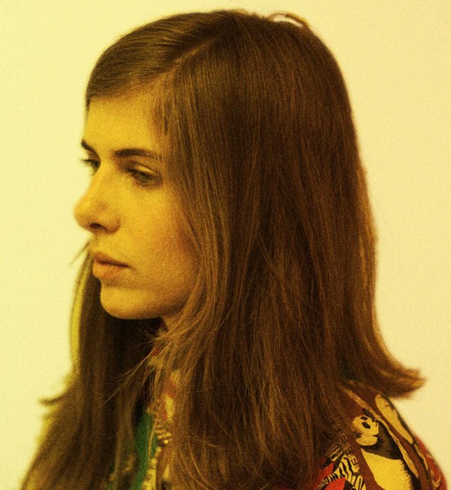 Profile portrait of Laurel Halo with shoulder-length brown hair against a pale yellow wall