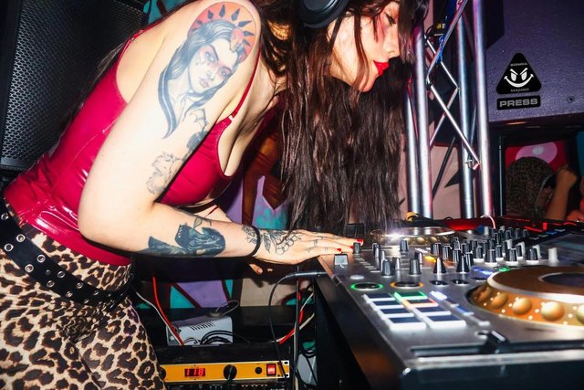 A DJ booth lit with violet lasers against a dark club interior