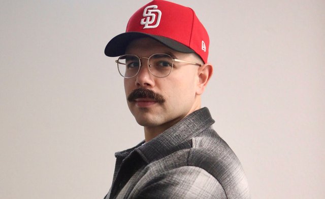 Bolo wearing a red San Diego cap and wire-frame glasses in a promotional portrait