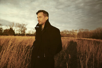 Bonobo standing in a field of tall dry grass at dusk wearing a dark coat