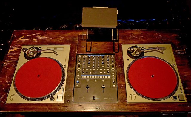 Two red-platter turntables and a mixer on a wooden DJ station