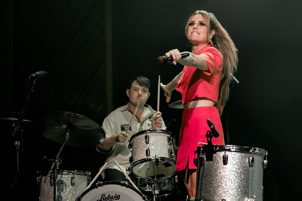 A singer reaches toward the crowd on stage at The Bellwether in Los Angeles, with a drummer behind her