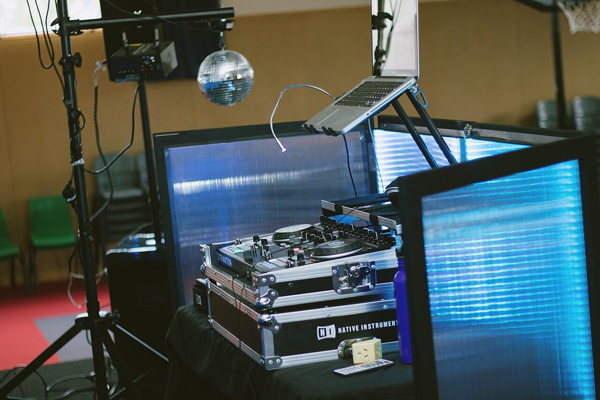 DJ equipment on a table beside a screen and mirror ball in a small club room