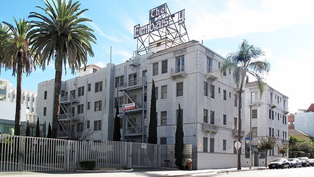 Corner view of a Koreatown apartment building with a rooftop sign, palm trees and a street lined with parked cars