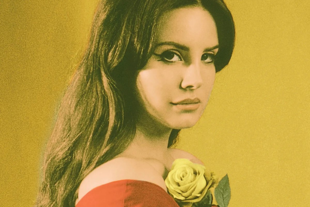 Lana Del Rey in a red off-shoulder top holding a yellow rose against a mustard-yellow backdrop