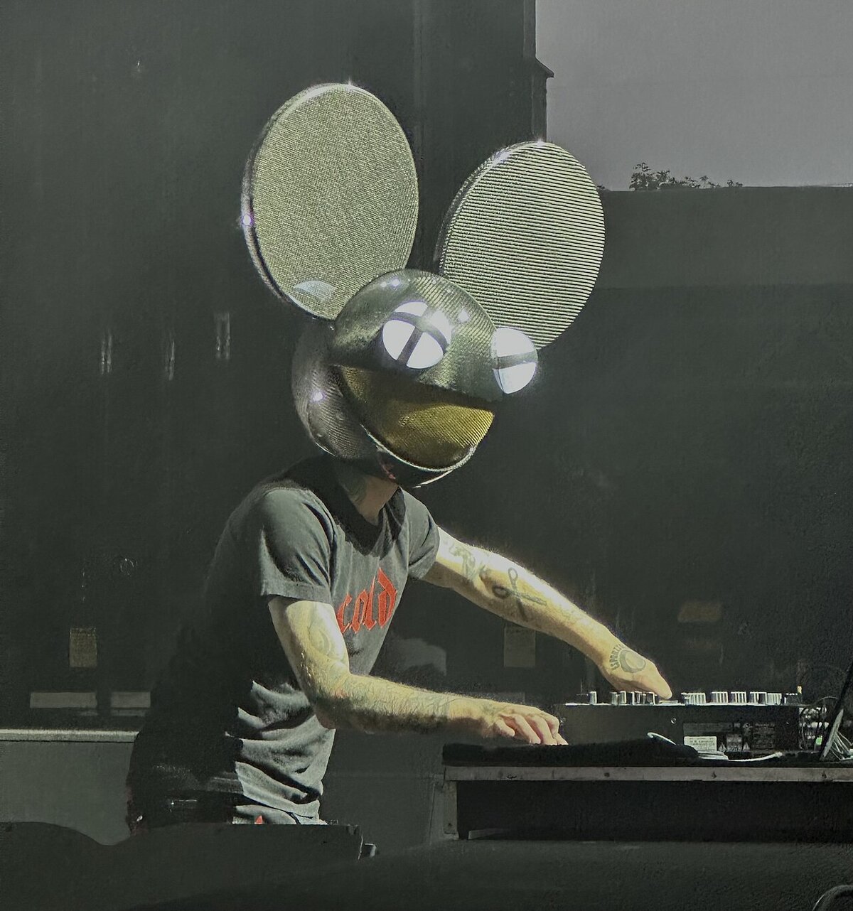 Deadmau5 in the mouse-head helmet with lit eyes, working a mixer at a DJ booth