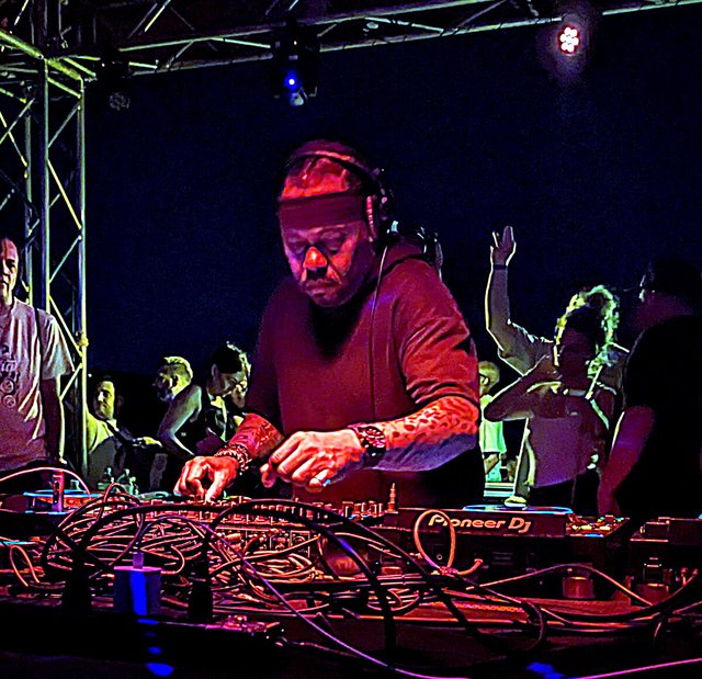 DJ in a headband and headphones working a Pioneer DJ mixer under stage lights with dancers behind