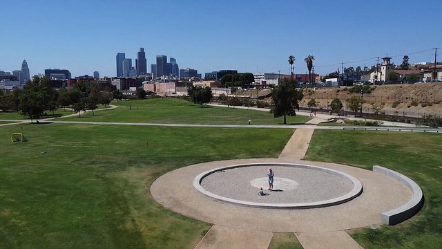 Grassy lawn and circular plaza at Los Angeles State Historic Park with the downtown skyline behind it