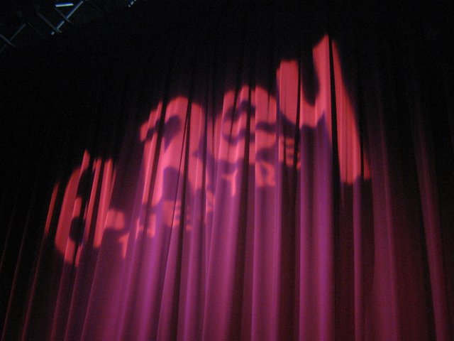 The El Rey Theatre's stage curtain lit pink and purple, with the venue's name projected in a soft spotlight across the folds