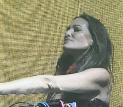 DJ Meredith Marks behind the decks during a live set, seen in profile against a glowing yellow LED screen