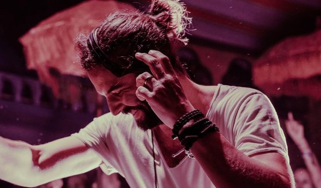 Eelke Kleijn smiling with one hand on his headphones while performing, lit in pink and red