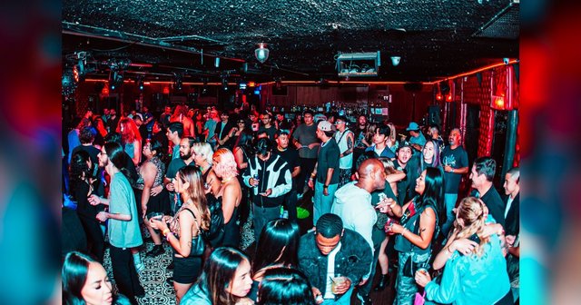 Dancers crowded together on the floor of a dimly lit club under red lighting
