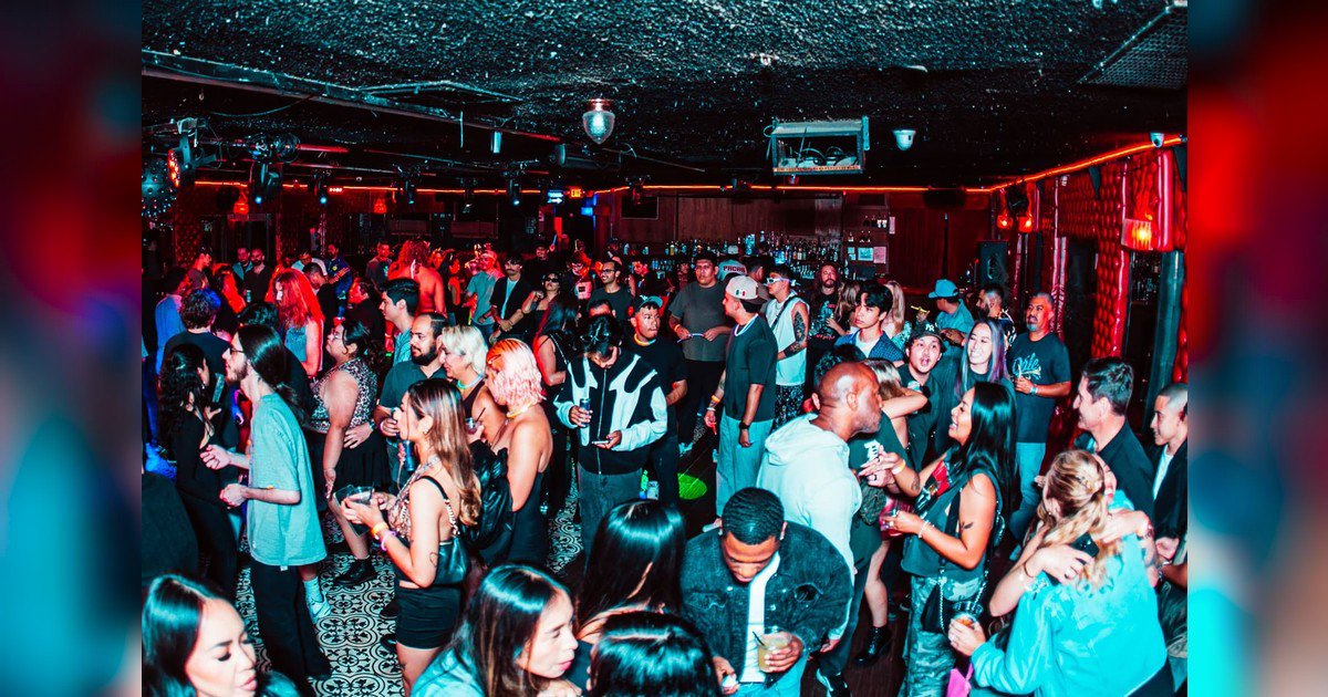 Dancers crowded together on the floor of a dimly lit club under red lighting
