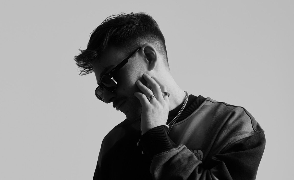 Black and white portrait of DJ Ely Oaks in sunglasses with a hand raised to his face