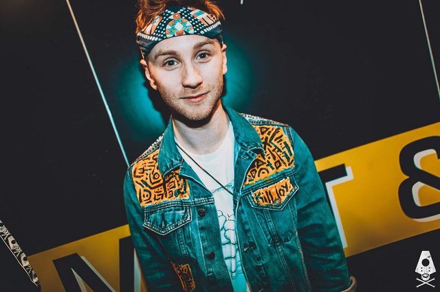 Fox Stevenson in a denim jacket and patterned bandana posing in front of a dark backdrop