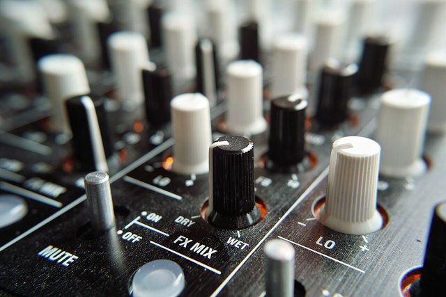 Close-up of a DJ mixer with rows of black and white knobs and faders