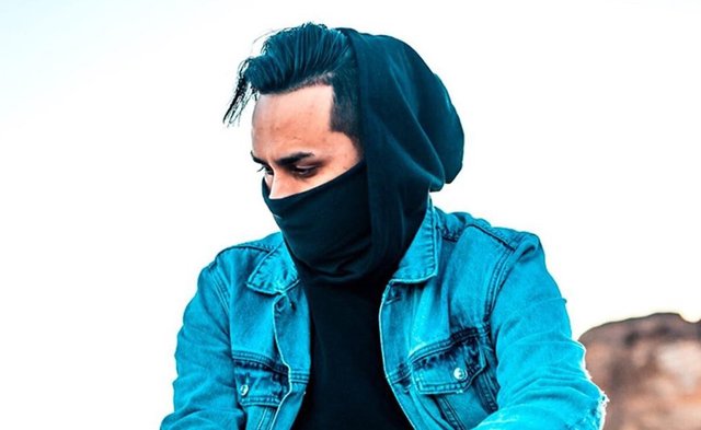 GEO in a hooded black face covering and denim jacket in a promotional portrait
