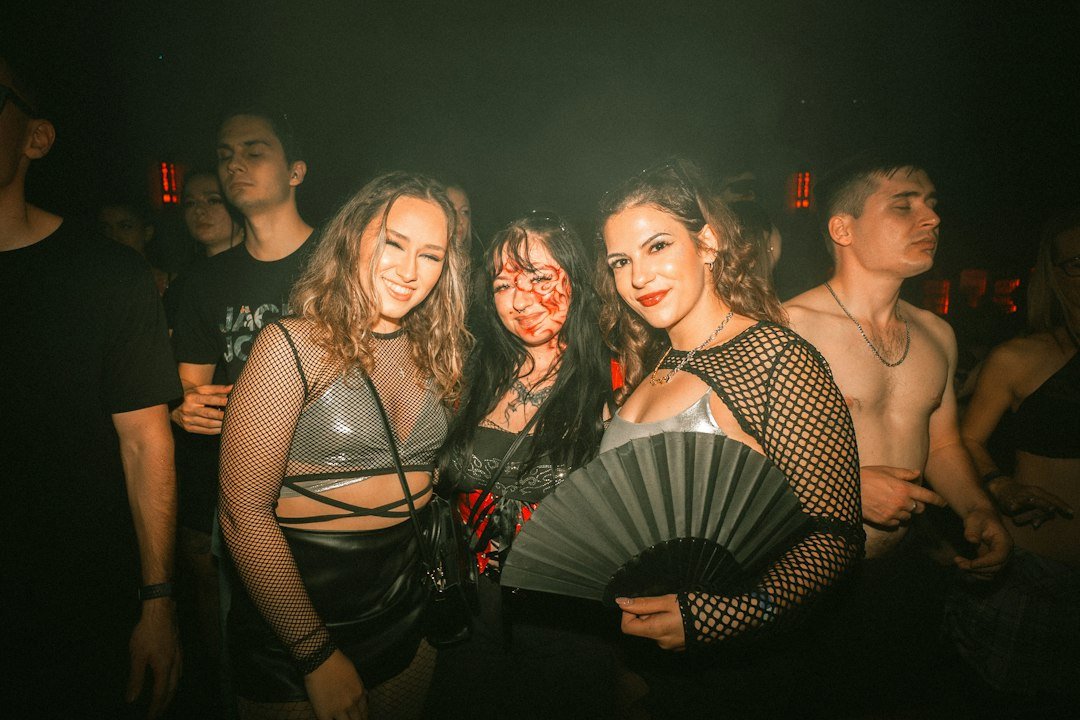Three women at a nighttime party under colorful lights, dressed up for a night out