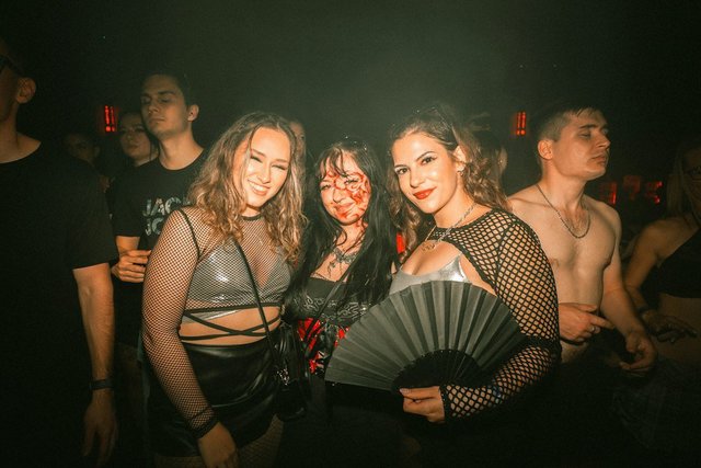 Three women at a nighttime party under colorful lights, dressed up for a night out
