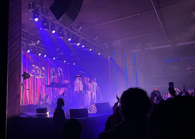 The stage inside The Bellwether in Los Angeles under purple and blue lighting rigs, with a crowd in silhouette raising their hands