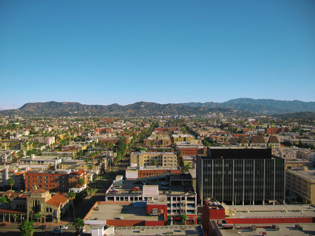 Aerial view of Koreatown rooftops and palm-lined streets with the Hollywood Hills under a clear blue sky