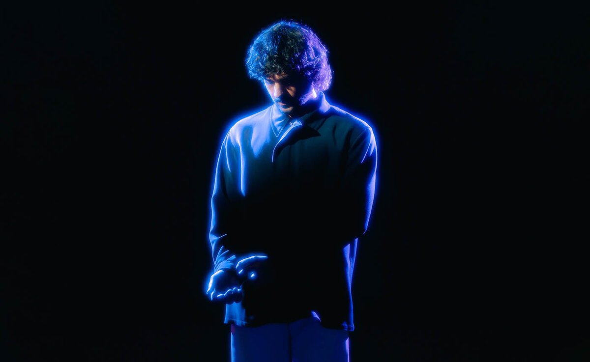 Jai Wolf standing in dark blue light with his head bowed