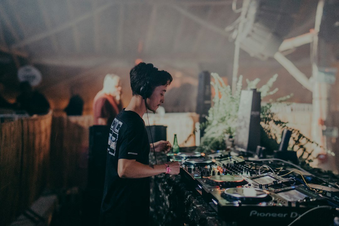 A DJ working at a mixing console under warm lighting at a live electronic music event